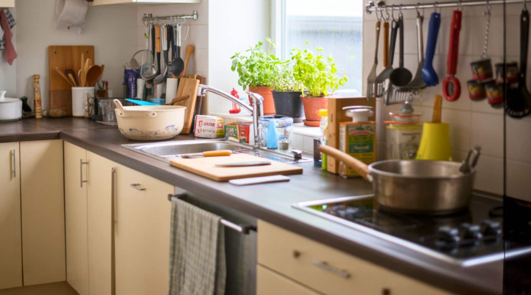 A small, lived-in home kitchen with a used countertop, pots on the stove, and everyday tools within reach